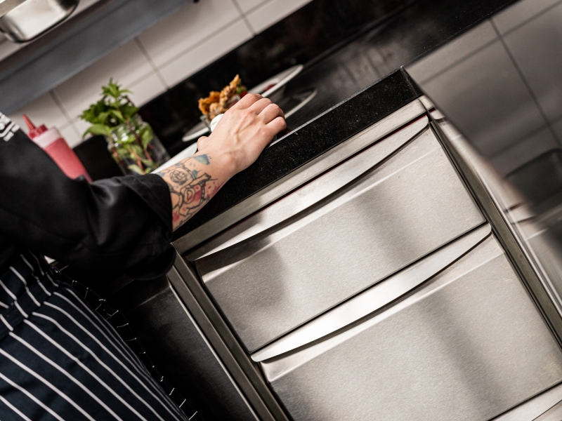 Edelstahl-Arbeitsschrank mit drei Laden und hygienischer Swingline Griffleiste abgedeckt mit schwarzer Granitplatte