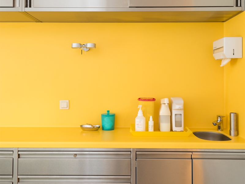 Arbeitsbereich in Ordination mit Edelstahlmöbeln und gelber Corian-Platte mit fugenlosem Wandhochzug über Eck