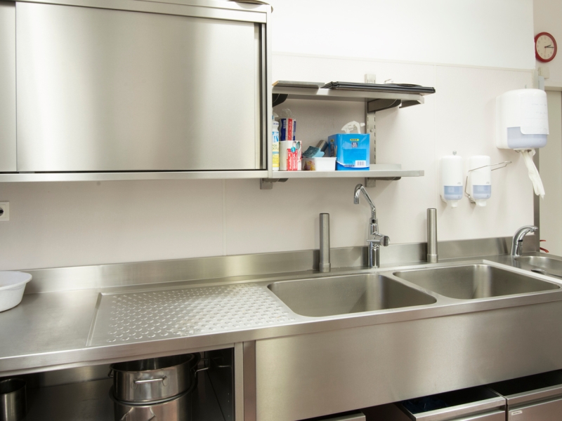 CNS-Verbau mit zwei großen Doppel-Waschbecken, gekantetem Wulstrand mit Gefälle und Tropfnoppen; Oberbei hängend: Wandhängeschrank mit Schiebetür, Wandbord zwei etagig