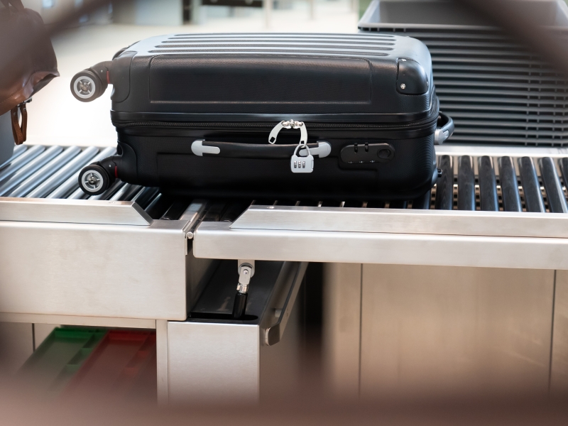 Schwarzer Koffer auf Rollbahn in Flughafen-Sicherheitskontrolle (inklusive Edelstahl-Klappboard für temporären Durchgang)