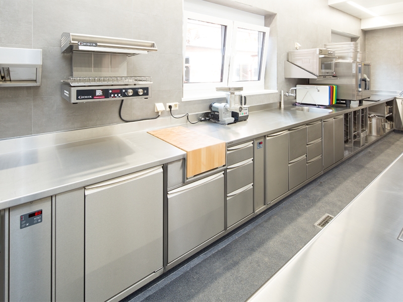 Wandzeile in Edelstahl mit fugenlosem Wandhochzug, bündig integriertem Hackblock und Unterbauten mit Metagro-Hygienegriffleiste